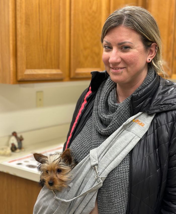 a women holding a small dog in a carrier in a kitchen
